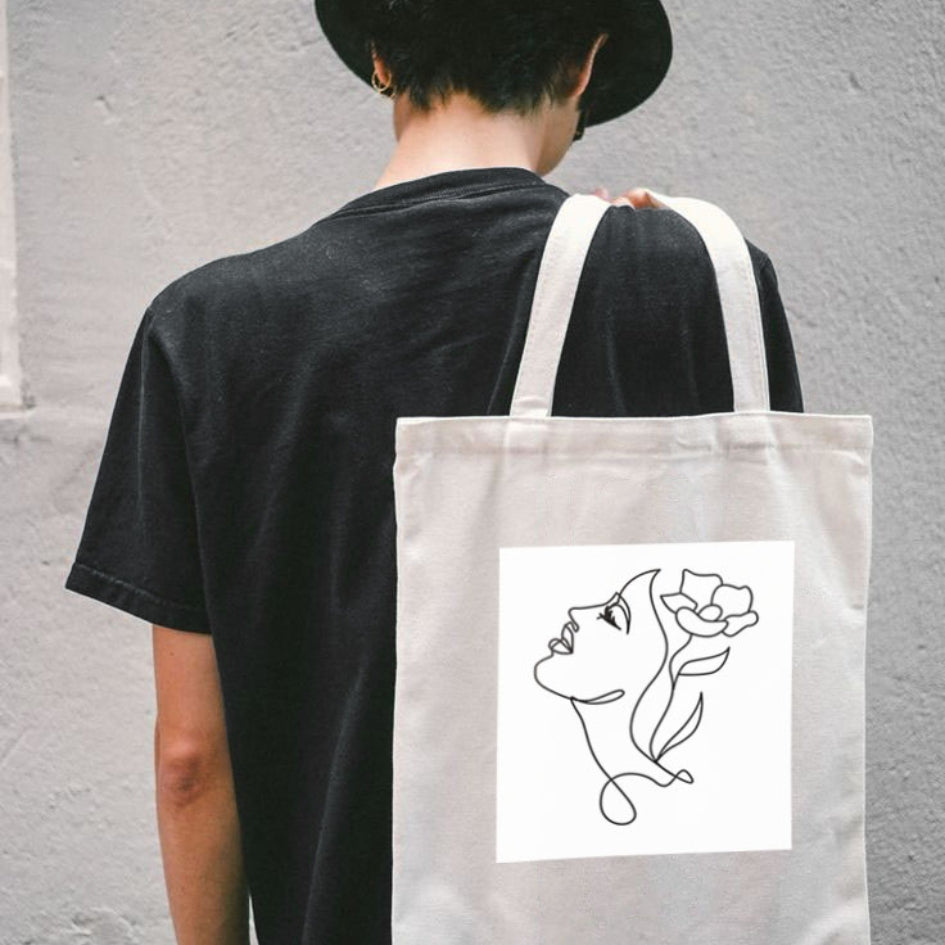 Plátená taška Kiskedves Line Art na chrbte, tvár s kvetom vo vlasoch, na postave v čiernom tričku.