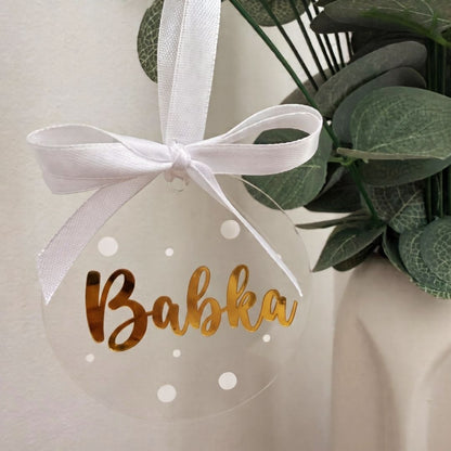 Priehľadná akrylová vianočná ozdoba so zlatým nápisom „Babka“, bielymi bodkami a saténovou mašľou