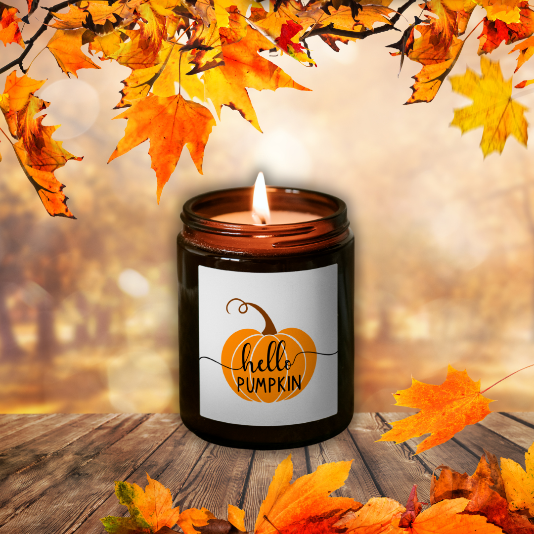 Horiaca sójová sviečka Pumpkin Spice v hnedom pohári so štítkom „hello PUMPKIN“, medzi jesenným lístím na drevenom stole