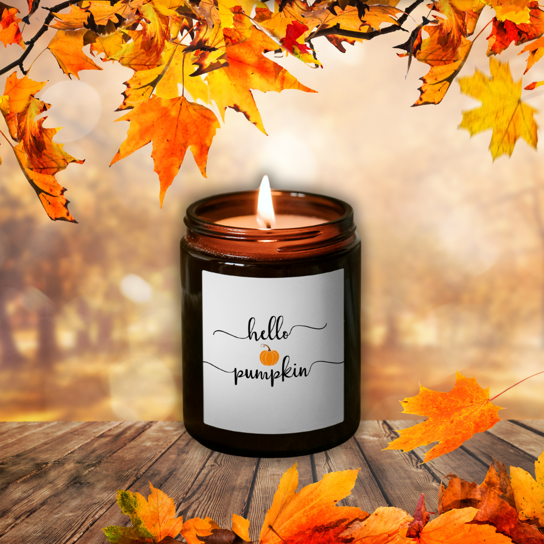 Horiaca sójová sviečka Pumpkin Spice v hnedom pohári so štítkom „hello pumpkin“, medzi jesenným lístím na drevenom stole