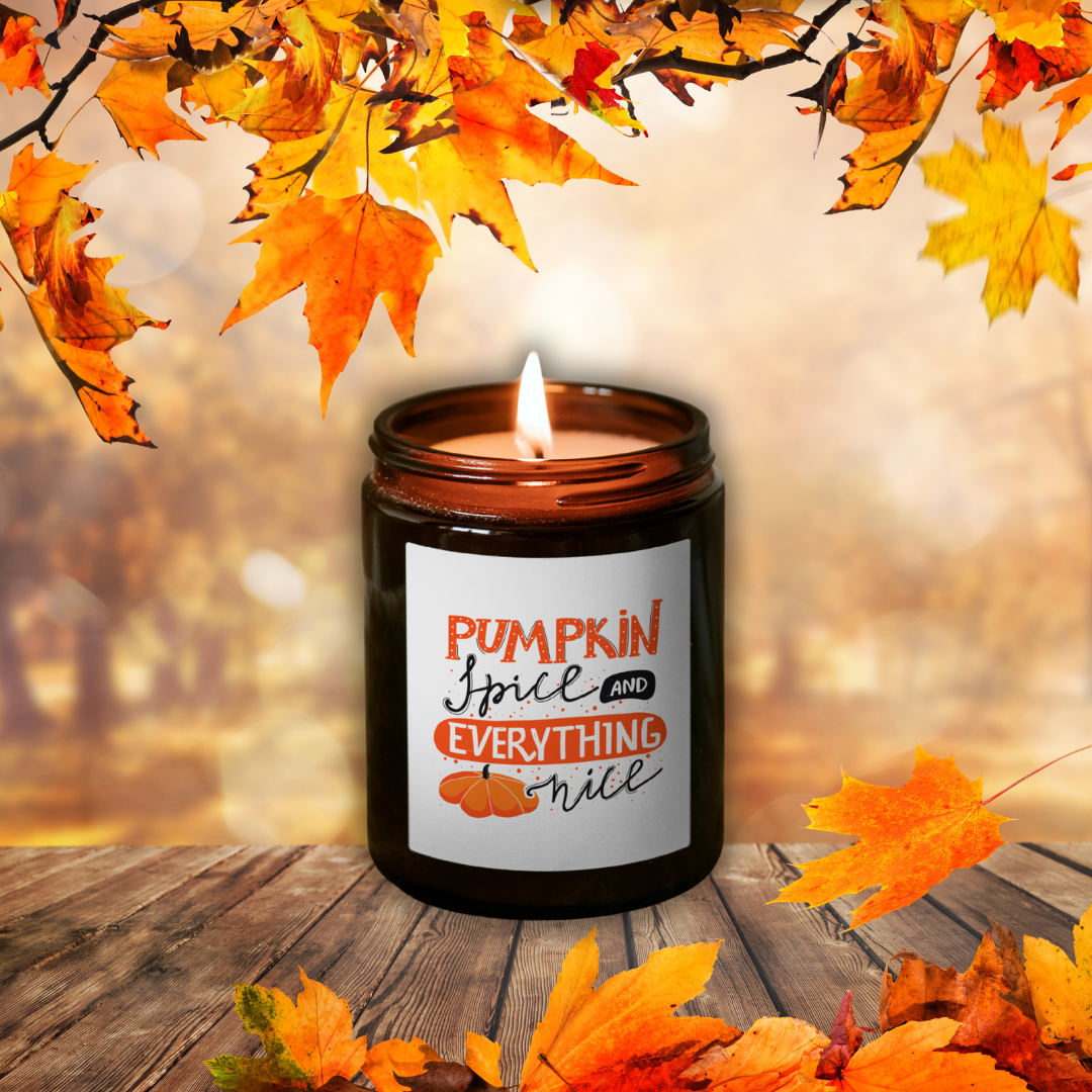 Horiaca sójová sviečka Pumpkin Spice v hnedom pohári so štítkom „Pumpkin Spice and everything nice“, medzi jesenným lístím na drevenom stole