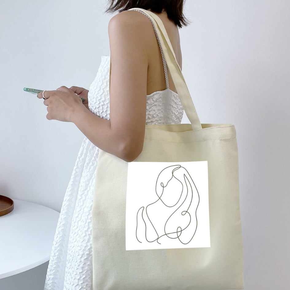 Plátená taška Kiskedves Line Art cez rameno, s prepletenými postavami, k bielym letným šatám.