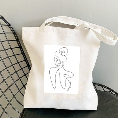 Plátená taška Kiskedves Line Art s postavou zozadu, na čiernej drôtenej stoličke.