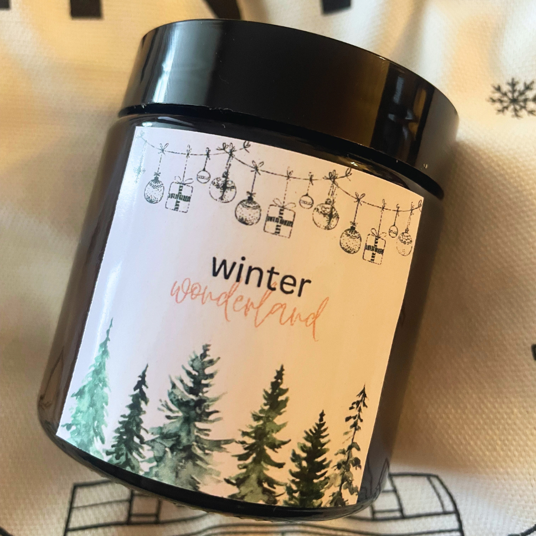 Sviečka Kiskedves Winter Wonderland na textílii so snehovými vločkami, zblízka so štítkom s lesom.