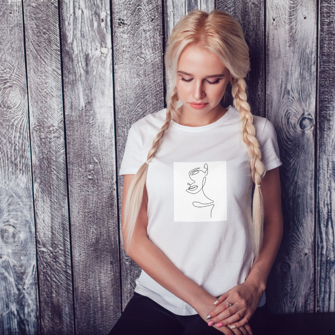 Biele tričko Kiskedves Line Art so ženským profilom, na modelke s vrkočmi pred drevenou stenou.