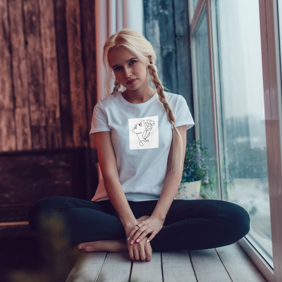 Biele tričko Kiskedves Line Art s kvetom vo vlasoch, na sediacej modelke pri okne.