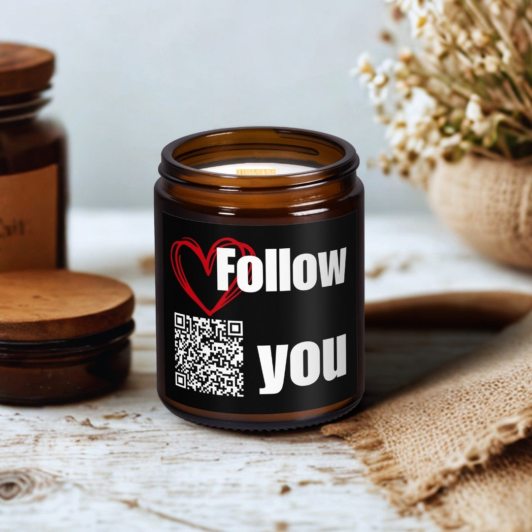 Sójová sviečka Kiskedves v hnedom sklenenom pohári s dreveným knôtom, na štítku QR kód a pieseň Follow You, na drevenom stole vedľa sušených kvetov