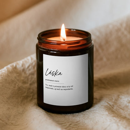 Horiaca sójová sviečka Kiskedves v hnedom pohári, na bielej etikete slovníkové heslo: „Láska, podstatné meno – To, keď ti prinesie kávu a ty nič nepovieš, aj keď sa nepodarila.“
