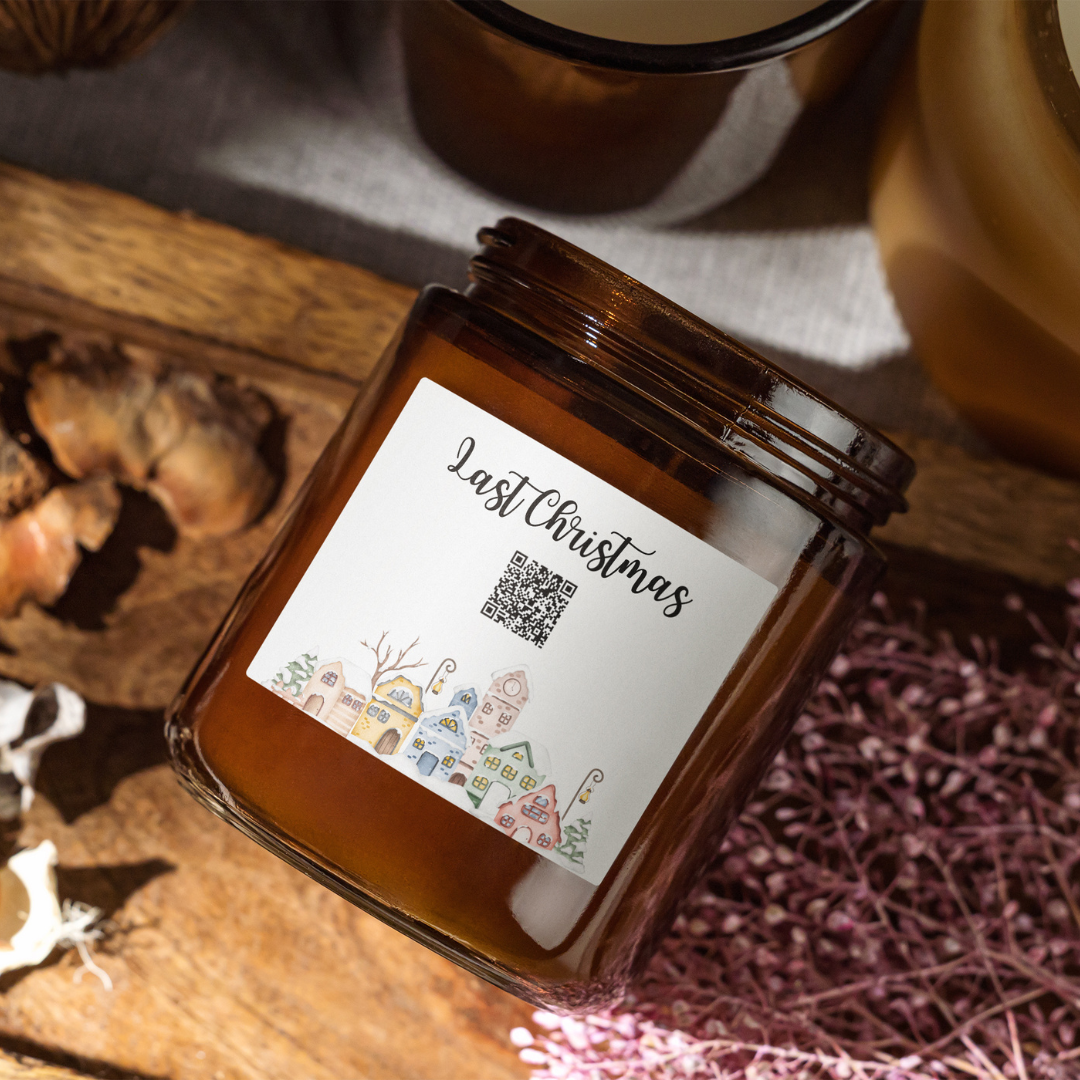 Vianočná sviečka „Melodická“ Kiskedves v hnedom pohári, na štítku QR kód a nápis Last Christmas