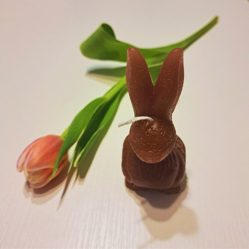 Sviečka Kiskedves v tvare zajačika z hnedého vosku s bielym knôtom, vo veľkonočnej dekorácii s tulipánmi.